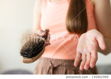Upset woman holding her brush with long loss hair. Closeup, selective focus. 130862999