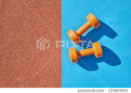 Orange dumbbells close-up and yoga mat at stadium 130863005