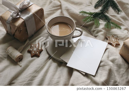 Winter still life. Cup of coffee, star gingerbread cookies. Linen table cloth. Gift box with ribbon, fir tree branch. Christmas breakfast, stationery. Blank greeting card, invitation mockup. Flatlay 130863267