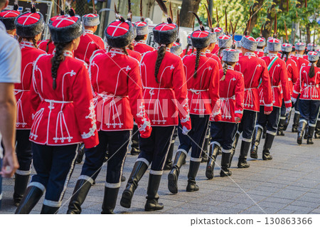 Group of Student Guards in red uniforms march in formation down the street with discipline and order. Concept of military parade, tradition, honor Group of Student Guards in red uniforms march in formation down the street with discipline and order. Concept of military parade, tradition, honor 130863366