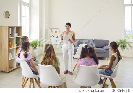 Friendly woman conducting psychological training for a group of school children girls. Friendly woman conducting psychological training for a group of school children girls. 130864638