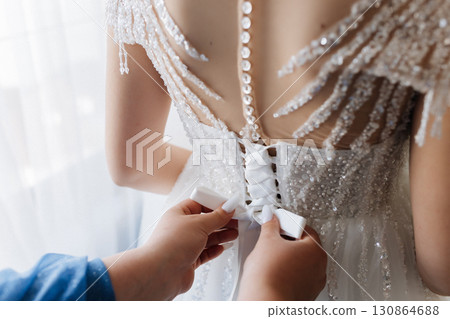 Hands tying elegant bridal dress with laces on wedding morning, close up preparation moment Hands tying elegant bridal dress with laces on wedding morning, close up preparation moment 130864688