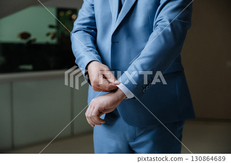 Man adjusting sleeve of blue suit, close-up, elegant formal style, indoors Man adjusting sleeve of blue suit, close-up, elegant formal style, indoors 130864689