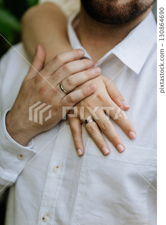 Close up of couple's hands with wedding and engagement rings on white shirt background Close up of couple's hands with wedding and engagement rings on white shirt background 130864690