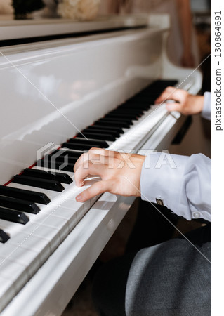 Man in white shirt playing white piano in natural light, close up of hands on keys Man in white shirt playing white piano in natural light, close up of hands on keys 130864691