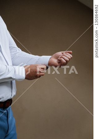 Man buttoning white shirt sleeve before event, cropped, minimal style Man buttoning white shirt sleeve before event, cropped, minimal style 130864692