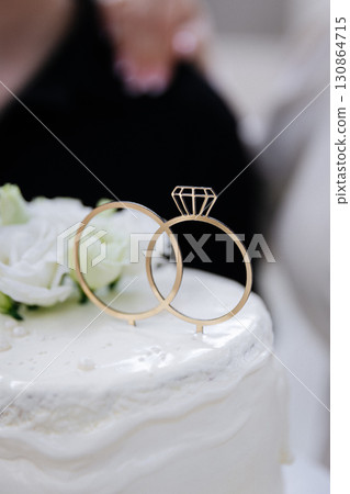 Wedding cake with floral decor and golden rings topper close up 130864715