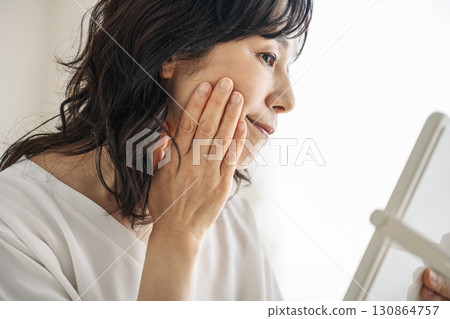 Middle-aged woman checking her skin in the mirror 130864757