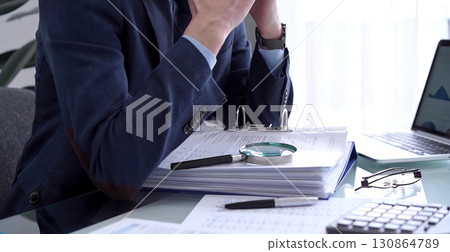 Businessman or auditor is looking through binders with papers while using a calculator and magnifying glass for financial documents analyzing. Audit and taxes concept 130864789