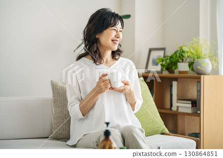 A middle-aged woman in her 50s relaxing on the sofa at home drinking coffee A middle-aged woman in her 50s relaxing on the sofa at home drinking coffee 130864851