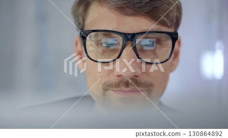 Businessman with glasses looking intently obscured partially by a translucent surface of laptop. Business concept Businessman with glasses looking intently obscured partially by a translucent surface of laptop. Business concept 130864892