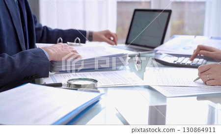 Business colleagues accountants or auditors reviewing financial data in office. Two professionals analyzing paper reports and using calculators. Audit and taxes Business colleagues accountants or auditors reviewing financial data in office. Two professionals analyzing paper reports and using calculators. Audit and taxes 130864911