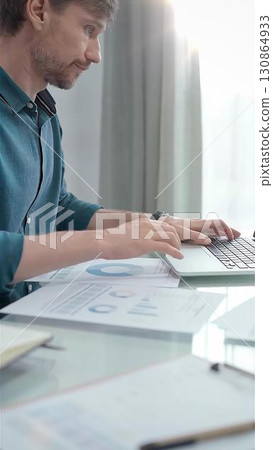 Entrepreneur wearing green shirt is working at laptop with data analysis charts in flair office. Vertical business portrait. Business people concept 130864933