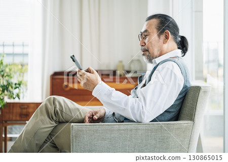 Senior man looking at smartphone on sofa at home Senior man looking at smartphone on sofa at home 130865015