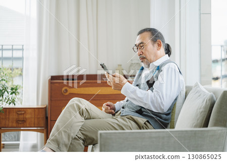 Senior man looking at smartphone on sofa at home 130865025