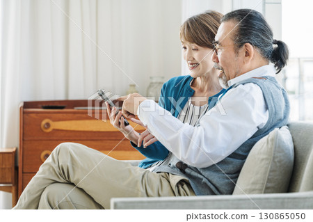 Senior couple looking at smartphone together in the living room at home Senior couple looking at smartphone together in the living room at home 130865050
