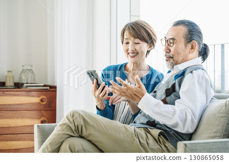 Senior couple looking at smartphone together in the living room at home 130865058