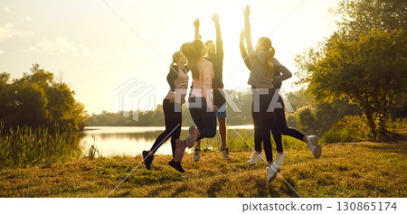 Group of people in sportswear standing in a circle jumping after sport workout in the park. Group of people in sportswear standing in a circle jumping after sport workout in the park. 130865174