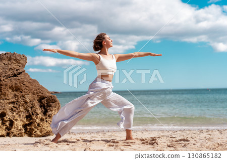 Young woman practicing Warrior Pose yoga on beach Young woman practicing Warrior Pose yoga on beach 130865182