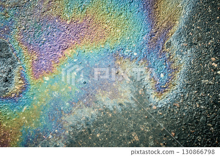 Rainbow oil spill creating an iridescent sheen on wet asphalt 130866798