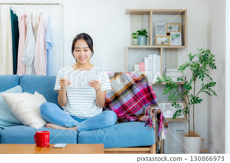 Young woman drinking coffee and looking at tablet in living room Young woman drinking coffee and looking at tablet in living room 130866973