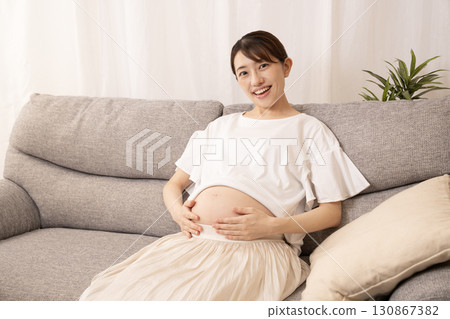 A pregnant woman sitting on a sofa and rubbing her stomach 130867382