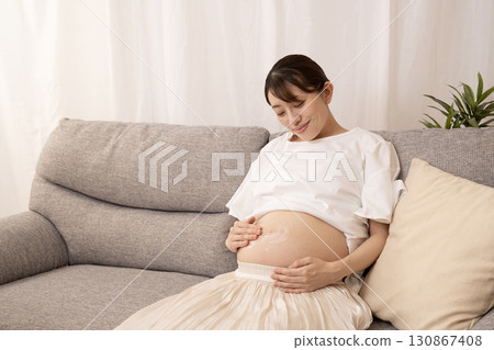 A pregnant woman applying cream to her enlarged belly 130867408