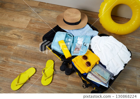 An open suitcase with clothes, cosmetics and travel accessories.  130868224
