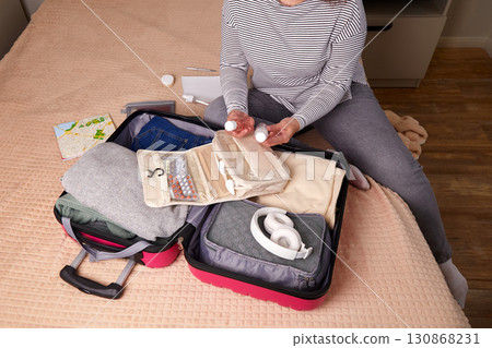 A woman puts hygiene products, clothes, a travel guide, headphones and travel accessories in a suitcase A woman puts hygiene products, clothes, a travel guide, headphones and travel accessories in a suitcase 130868231