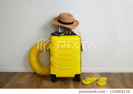 On yellow suitcase there is a straw hat and travel documents.  130868238