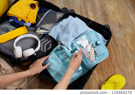 A woman puts hygiene products, clothes, a travel guide, headphones and travel accessories in a suitcase 130868278
