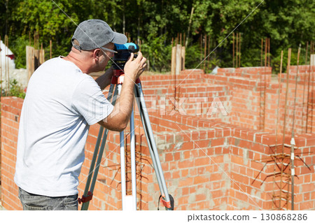 A construction worker checks the height level of the brickwork using a measuring tool on the construction site.  130868286