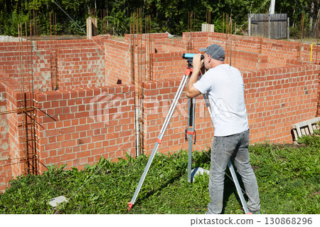 A construction worker checks the height level of the brickwork using a measuring tool on the construction site. A construction worker checks the height level of the brickwork using a measuring tool on the construction site. 130868296
