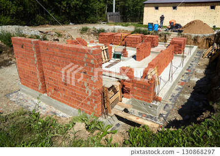 Workers are building solid brick walls of a house in a quiet suburban neighborhood.  130868297