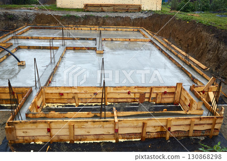 Construction of a concrete foundation with wooden forms at a building site on a cloudy day Construction of a concrete foundation with wooden forms at a building site on a cloudy day 130868298