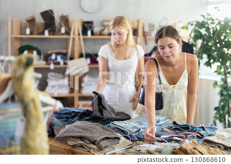 Fashionista girls near showcase examine goods, buying shorts or trousers Fashionista girls near showcase examine goods, buying shorts or trousers 130868610