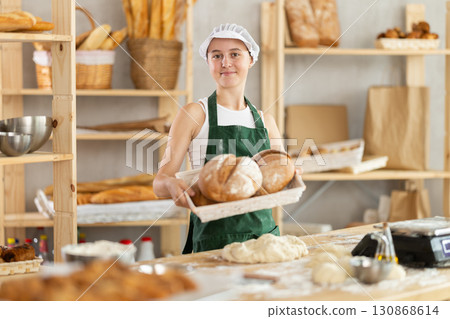 Young girl baker are standing near product range in bakery kitchen with basket loaf of bread 130868614
