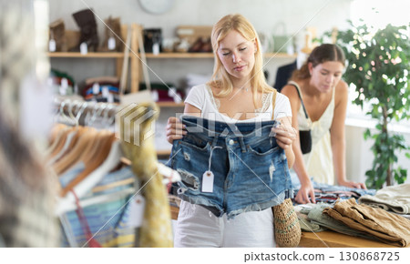 Fashionista girl buying denim shorts. Female client choosing something in background 130868725