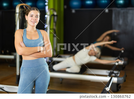 Female trainer stands in gym against background of Pilates reformer machines 130868762