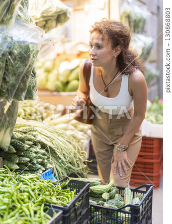 Woman inspecting fresh greens at street-side vegetable stall 130868803