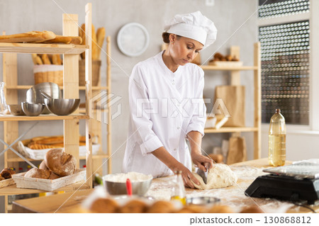 Adult woman baker cutting dough with scraper 130868812