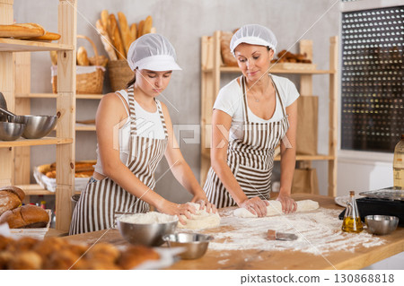 Two bakery employees work together to prepare dough for baking baguettes and croissants Two bakery employees work together to prepare dough for baking baguettes and croissants 130868818