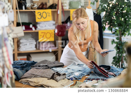 Young female customer scans QR code on trousers or shorts label 130868884