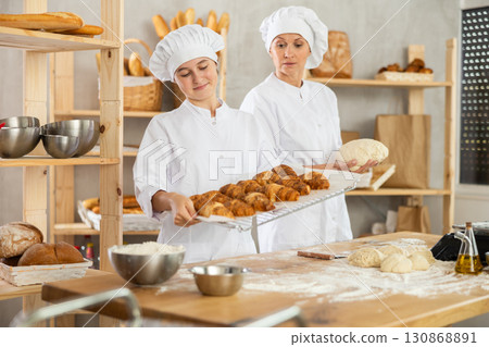 Female bakers rolling out dough and chatting 130868891
