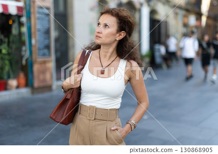 Serious middle-aged woman walking along square 130868905