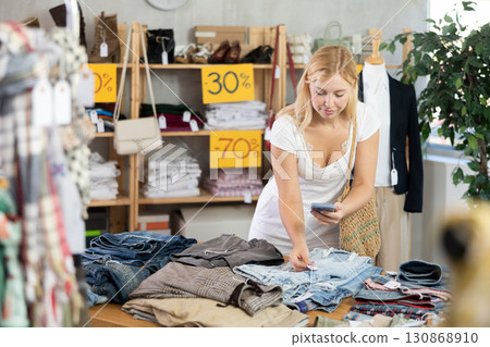 Young female customer scans QR code on trousers or shorts label 130868910