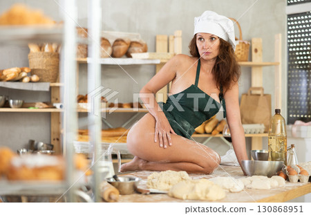 Woman in apron kneeling on table in bakery Woman in apron kneeling on table in bakery 130868951