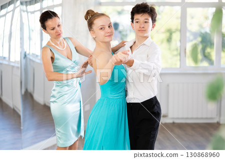 Girl and a boy in festive clothes learn to dance tango under guidance of teacher Girl and a boy in festive clothes learn to dance tango under guidance of teacher 130868960