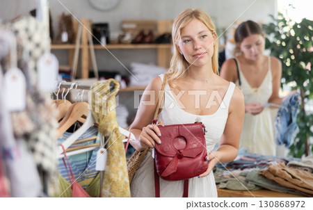 Young girl near showcase examine goods, buying handbag. Client looking for something in background 130868972