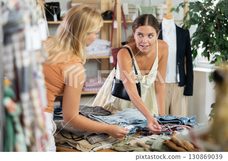 Fashionista girls near showcase examine goods, buying shorts or trousers 130869039